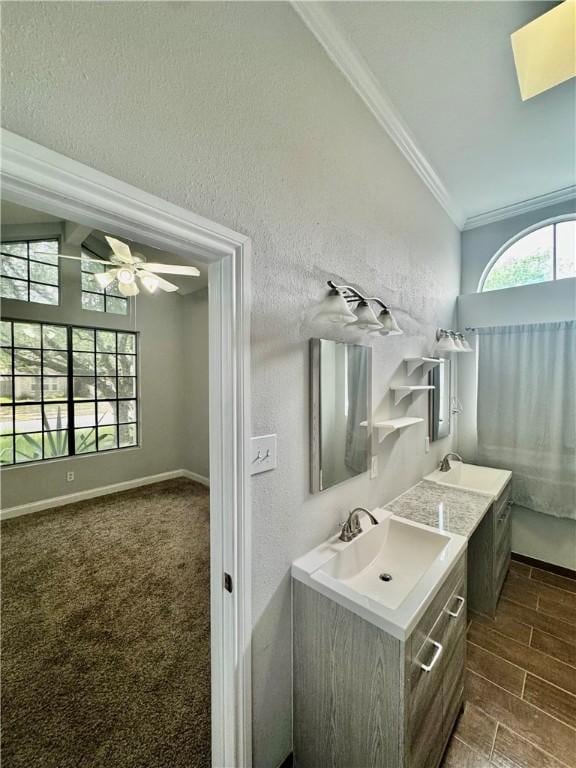 full bathroom featuring ceiling fan, crown molding, vanity, baseboards, and a textured wall