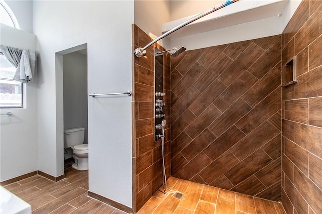 bathroom with toilet, tiled shower, and wood finished floors