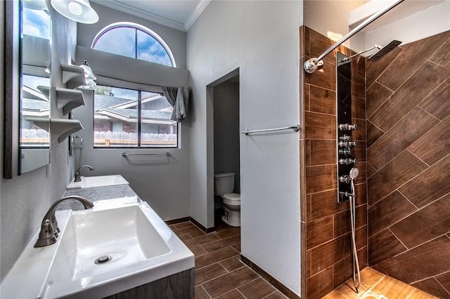 bathroom featuring a sink, crown molding, a tile shower, and toilet