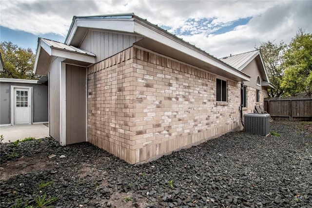 view of side of home featuring central air condition unit, fence, and metal roof