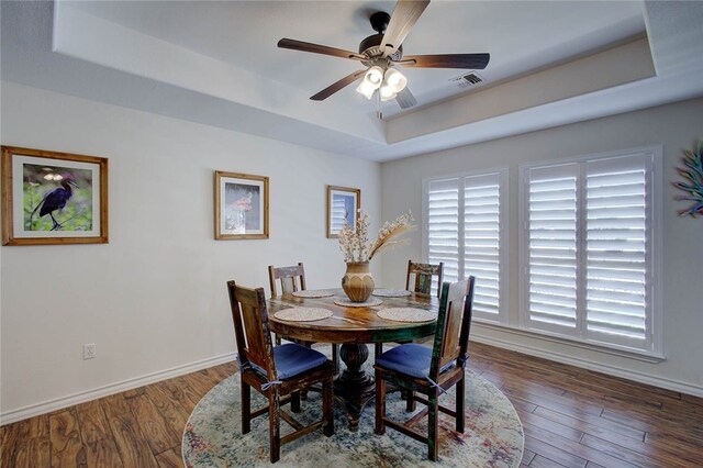 dining room featuring dark wood-type flooring, a tray ceiling, and ceiling fan