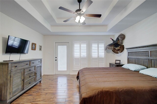 bedroom featuring light hardwood / wood-style floors, ceiling fan, and a raised ceiling