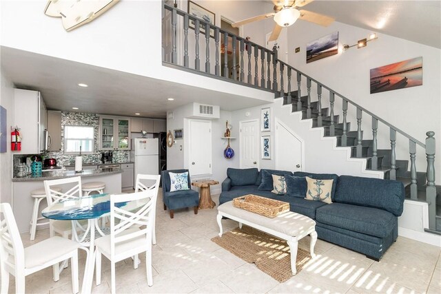 living room with stairway, ceiling fan, visible vents, and a towering ceiling