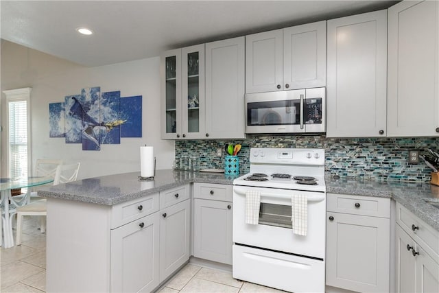 kitchen featuring stainless steel microwave, glass insert cabinets, light tile patterned floors, a peninsula, and white range with electric stovetop