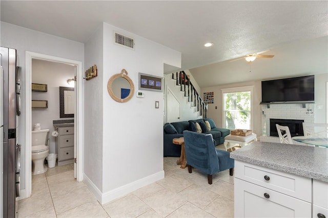 living area with stairway, a ceiling fan, visible vents, light tile patterned flooring, and a fireplace