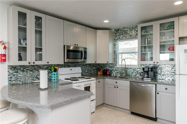 kitchen featuring a sink, light stone counters, tasteful backsplash, stainless steel appliances, and a peninsula