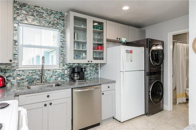 kitchen featuring stacked washer and clothes dryer, a sink, backsplash, white appliances, and glass insert cabinets