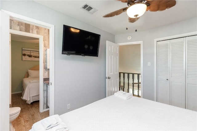 bedroom featuring wood finished floors, visible vents, ensuite bath, ceiling fan, and a closet
