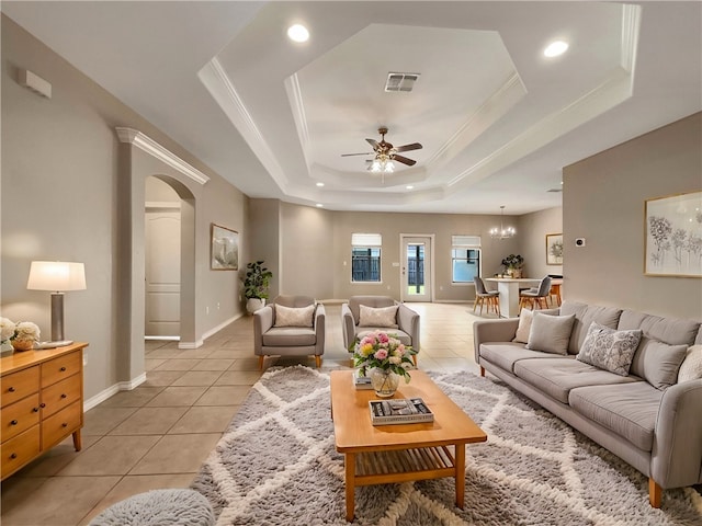 living room with crown molding, ceiling fan with notable chandelier, light tile patterned flooring, and a raised ceiling