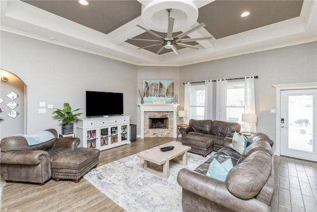 living room with coffered ceiling, a stone fireplace, light hardwood / wood-style flooring, ornamental molding, and ceiling fan