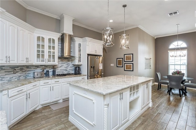 kitchen featuring appliances with stainless steel finishes, pendant lighting, white cabinets, a center island, and wall chimney exhaust hood