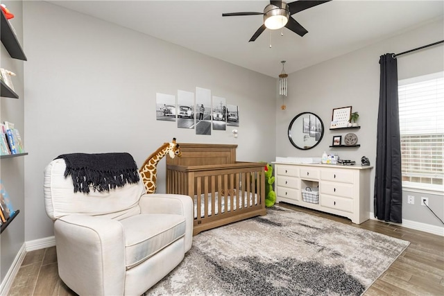 bedroom with ceiling fan, a crib, and wood-type flooring