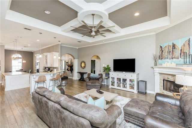 living room featuring coffered ceiling, ceiling fan with notable chandelier, ornamental molding, and light wood-type flooring