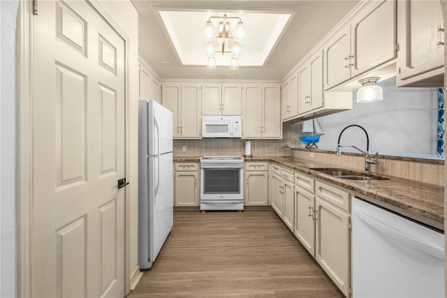 kitchen with sink, a tray ceiling, light stone countertops, light hardwood / wood-style flooring, and white appliances