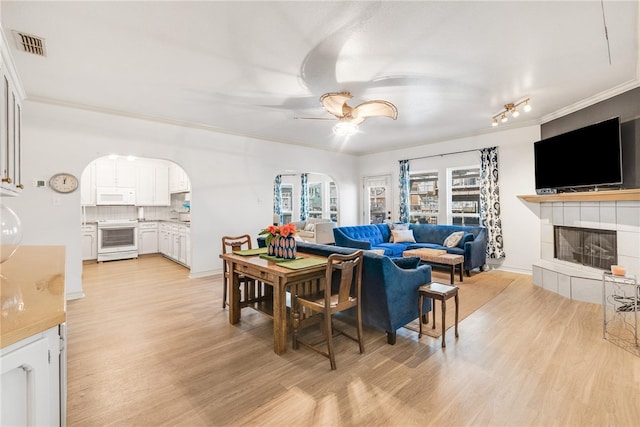 living room featuring ceiling fan, a tile fireplace, light wood-type flooring, and crown molding