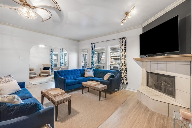 living room featuring ceiling fan, light hardwood / wood-style floors, a tiled fireplace, and ornamental molding