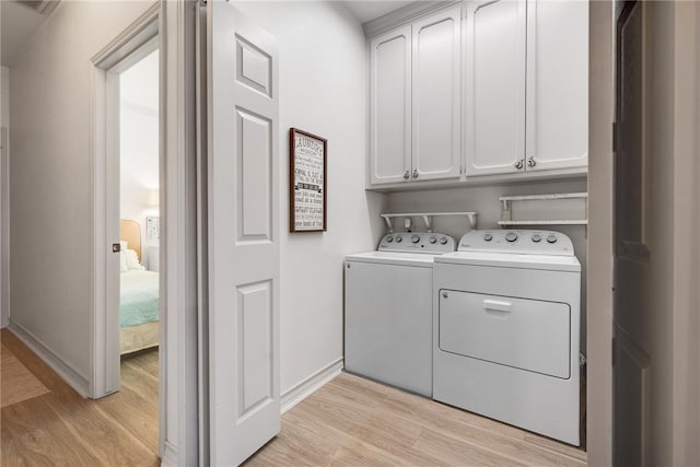 clothes washing area featuring washer and clothes dryer, cabinets, and light hardwood / wood-style floors