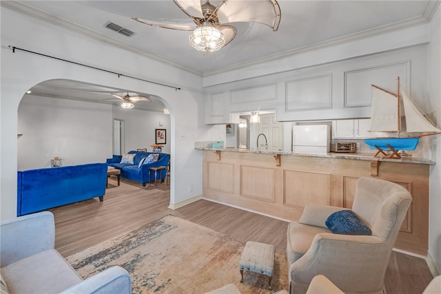 living room featuring ceiling fan, sink, crown molding, and light hardwood / wood-style flooring