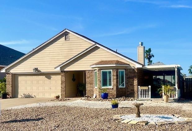 single story home featuring an attached garage, a chimney, driveway, and brick siding