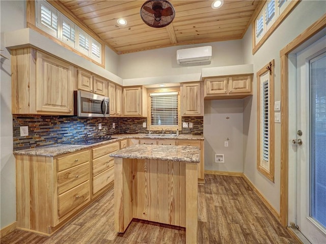 kitchen with black electric stovetop, light brown cabinets, an AC wall unit, a center island, and stainless steel microwave