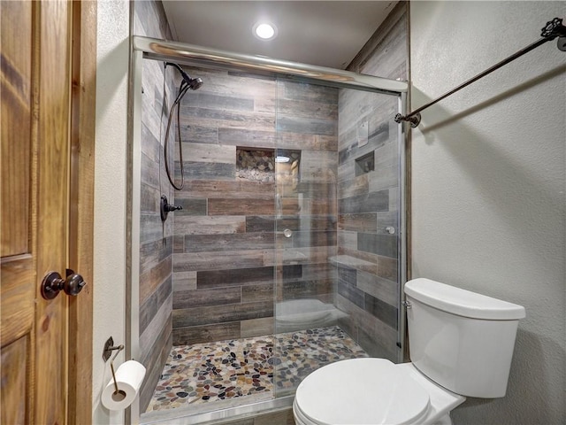 full bathroom with a textured wall, a shower stall, and toilet