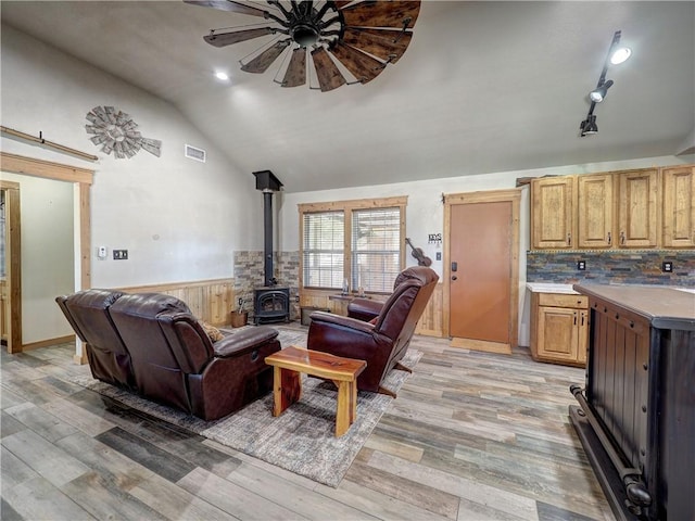 living room with light wood-style flooring, a wainscoted wall, visible vents, vaulted ceiling, and a wood stove