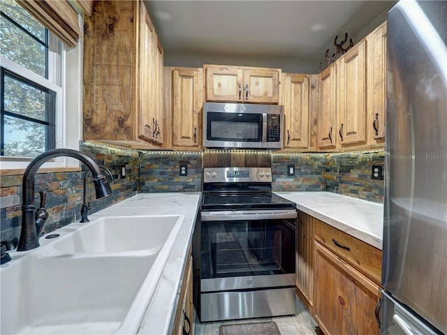 kitchen with backsplash, appliances with stainless steel finishes, light countertops, and a sink