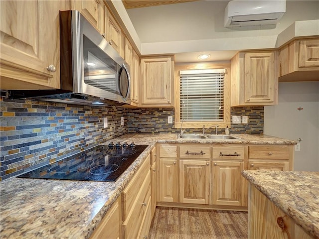 kitchen with stainless steel microwave, black electric stovetop, light brown cabinetry, a sink, and a wall mounted AC