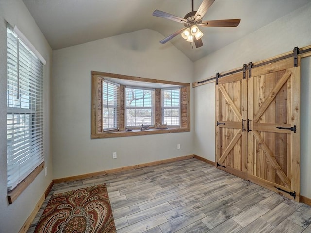 unfurnished room with vaulted ceiling, a barn door, light wood finished floors, and plenty of natural light