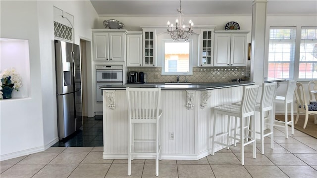 kitchen with glass insert cabinets, stainless steel fridge with ice dispenser, tasteful backsplash, dark countertops, and decorative light fixtures