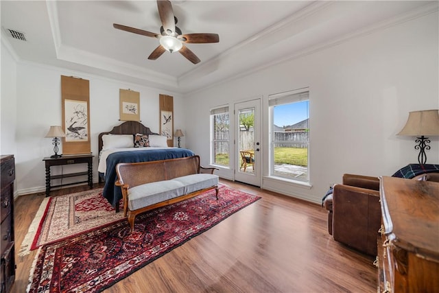 bedroom featuring ceiling fan, access to outside, hardwood / wood-style flooring, and a tray ceiling