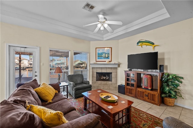 living room featuring a tiled fireplace, light tile patterned floors, ceiling fan, and a raised ceiling