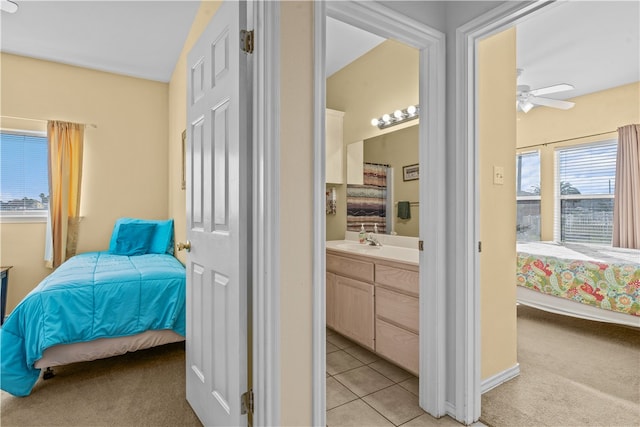 bedroom with ceiling fan, ensuite bathroom, light colored carpet, and sink