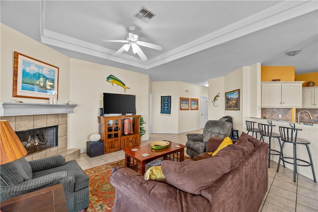 tiled living room featuring ceiling fan, a raised ceiling, and a tile fireplace