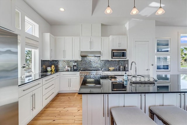 kitchen featuring pendant lighting, white cabinets, a breakfast bar area, and built in appliances