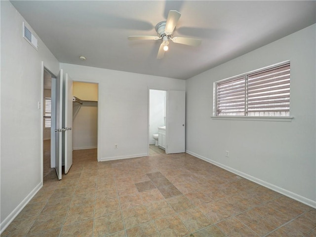 unfurnished bedroom featuring ceiling fan, a walk in closet, ensuite bathroom, and a closet