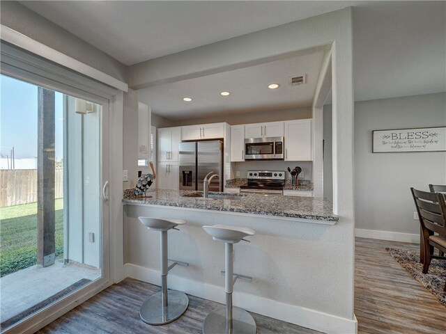 kitchen with white cabinetry, light wood-type flooring, stainless steel appliances, and light stone counters