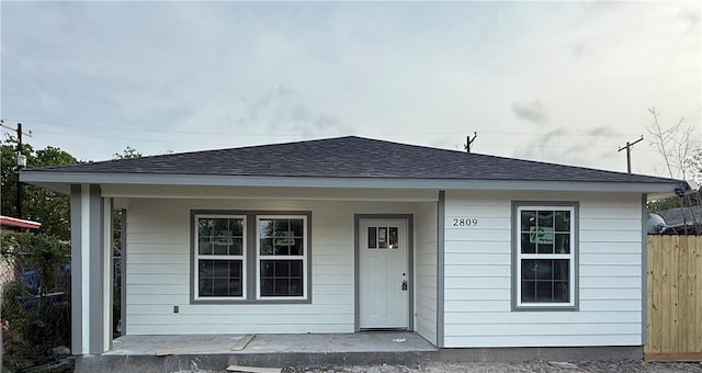bungalow featuring a porch, a shingled roof, and fence