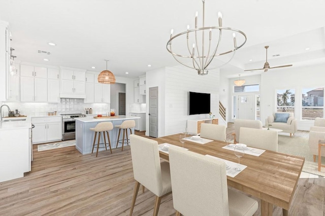 dining space with ceiling fan with notable chandelier, sink, and light hardwood / wood-style flooring