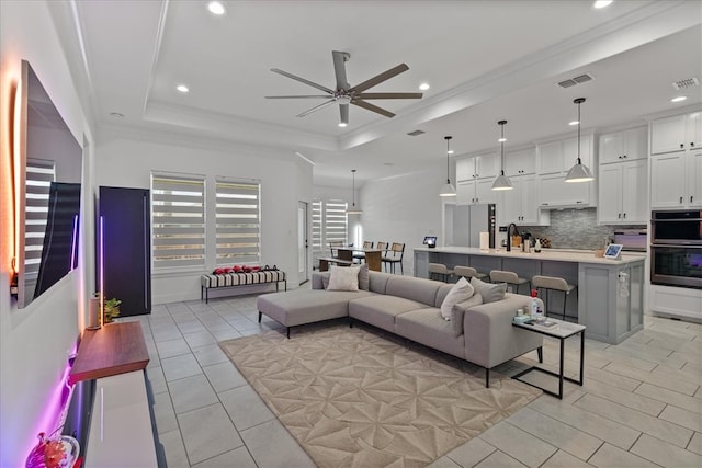 living room featuring sink, crown molding, ceiling fan, and a raised ceiling