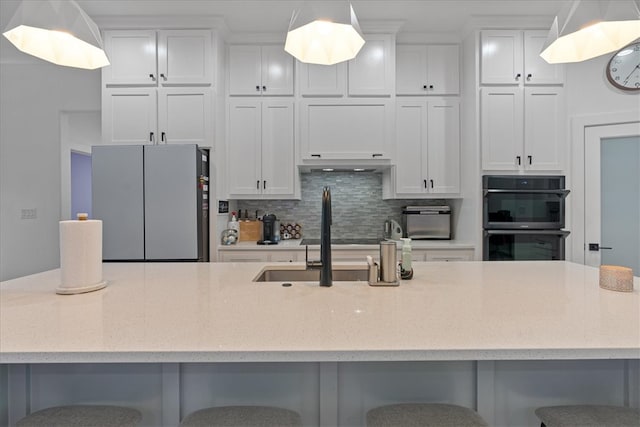 kitchen featuring stainless steel fridge, decorative backsplash, white cabinets, a breakfast bar area, and double oven