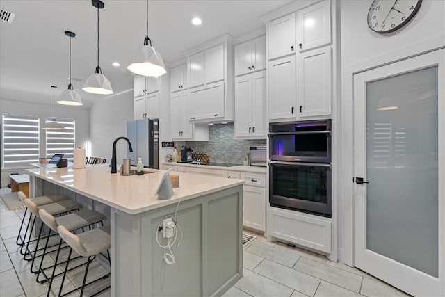 kitchen featuring black appliances, pendant lighting, an island with sink, and white cabinets