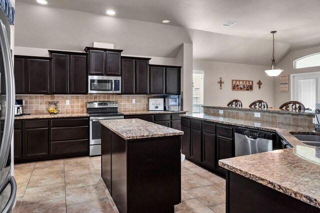 kitchen featuring tasteful backsplash, stainless steel appliances, decorative light fixtures, a center island, and lofted ceiling