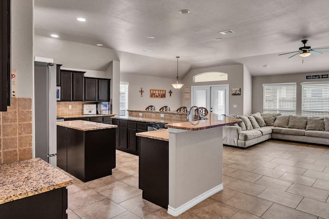 kitchen featuring light stone countertops, pendant lighting, lofted ceiling, and an island with sink