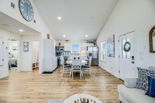 dining area featuring light wood-style flooring, recessed lighting, visible vents, and high vaulted ceiling