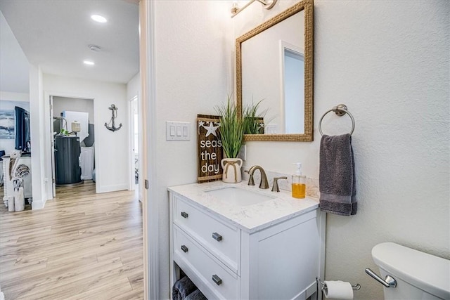 half bathroom with toilet, wood finished floors, recessed lighting, baseboards, and vanity