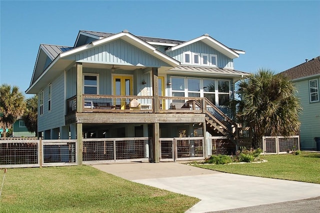 raised beach house with a front lawn, fence, a standing seam roof, metal roof, and a ceiling fan