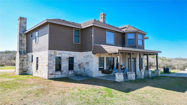 back of property featuring a patio, a chimney, a yard, and stone siding