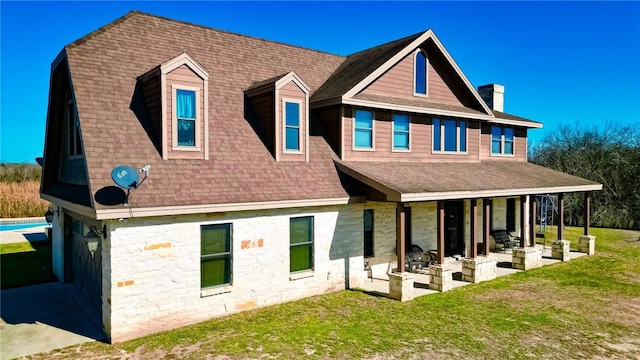 back of house with a lawn, a shingled roof, and a patio area