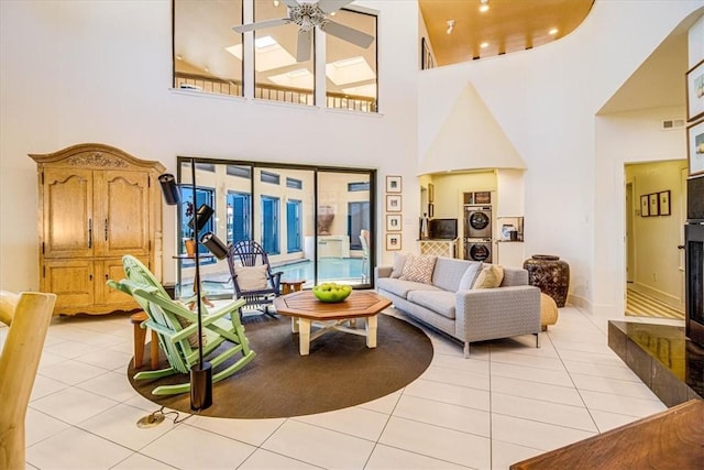 living area with stacked washer and dryer, a fireplace with raised hearth, ceiling fan, and light tile patterned floors